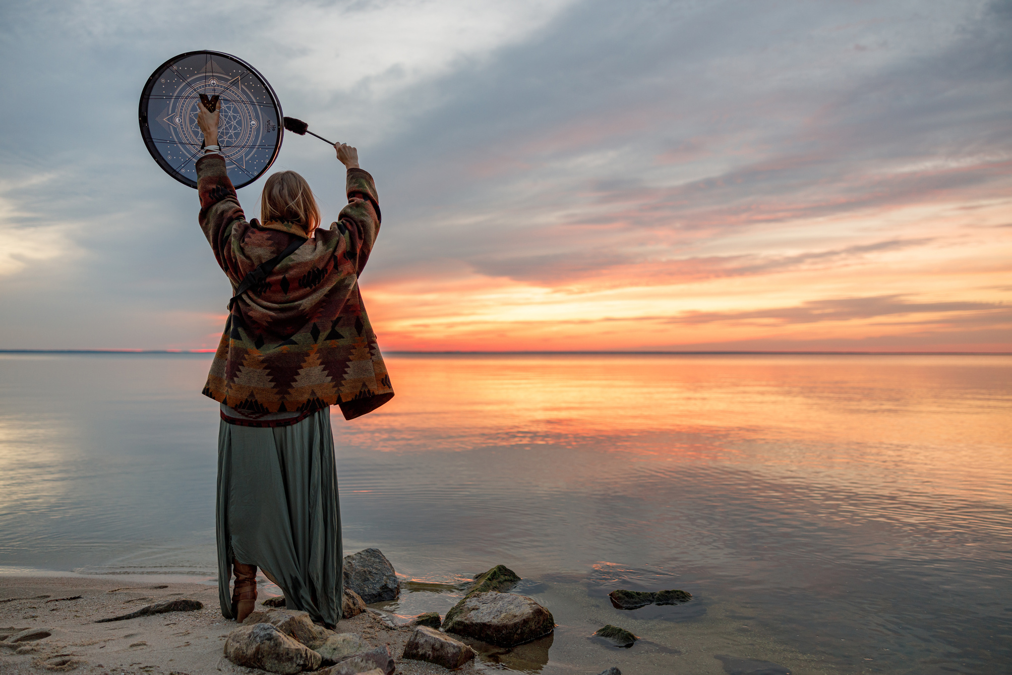 Young ethnic mature shaman female is walking and playing drums meditative music